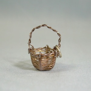 May include: A silver wire basket charm with a twisted wire handle. The basket is woven with a fine wire and has a delicate, intricate design.