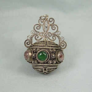 May include: A silver filigree pendant featuring a round, green and pink gemstone design. The pendant has a delicate, intricate design and is perfect for adding a touch of elegance to any outfit.