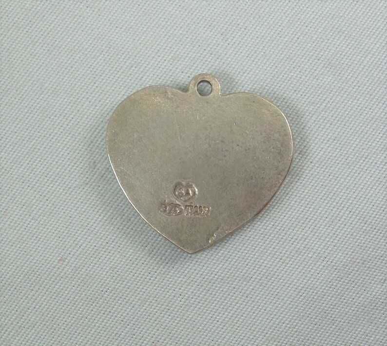 May include: Silver heart-shaped pendant with a small inscription on the back. The inscription reads "925 Italy".
