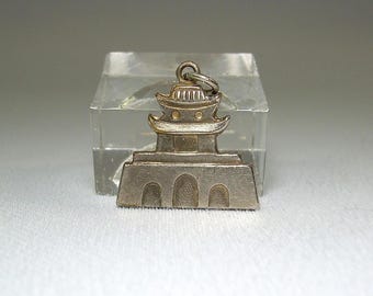 May include: Silver charm in the shape of a pagoda with a gold roof. The charm is detailed with arches and windows.