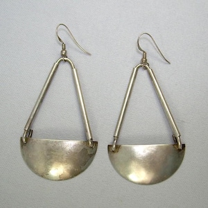 May include: A pair of silver earrings with a triangular shape and a half-circle pendant. The earrings are made of a smooth, polished metal.