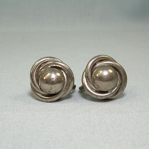 May include: A pair of silver earrings with a knotted design and a round center.