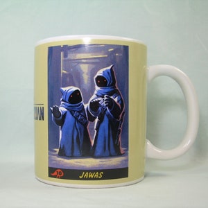May include: A white ceramic mug with a yellow background and a picture of two blue-robed Jawas from Star Wars. The text "JAWA'S" is printed below the image.