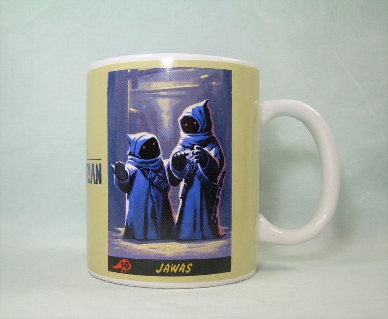 May include: A white ceramic mug with a yellow background and a picture of two blue-robed Jawas from Star Wars. The text "JAWA'S" is printed below the image.