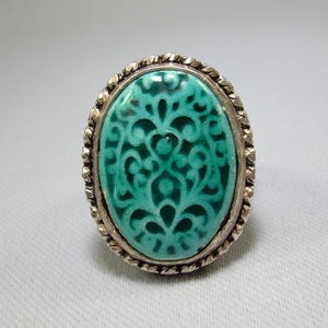 May include: A silver ring with a turquoise oval-shaped stone featuring a carved floral design.