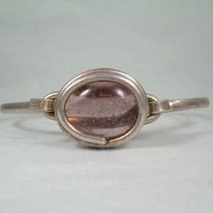 May include: A silver bangle bracelet with a light purple glass cabochon set in a silver bezel.