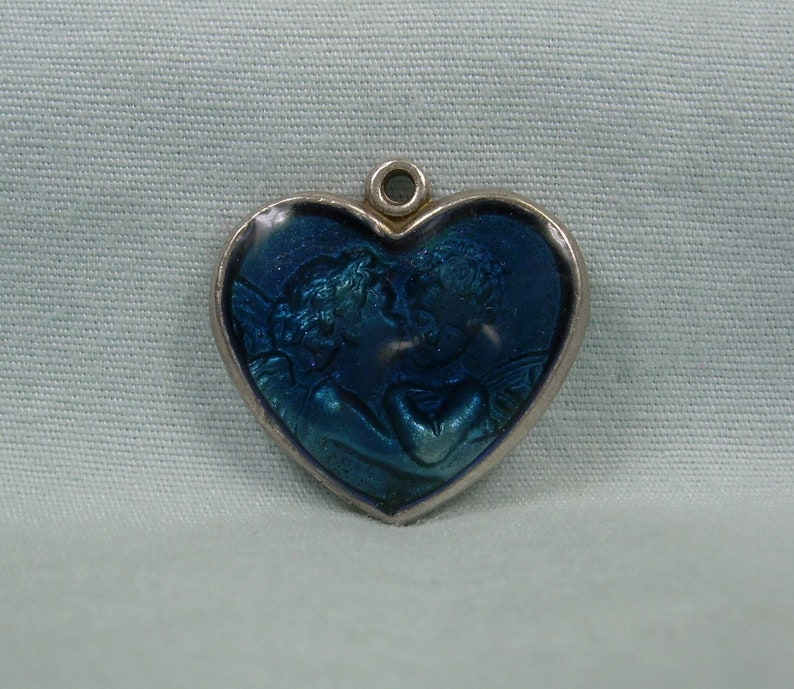 May include: A silver heart-shaped charm with a blue enamel design of two angels embracing.