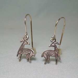 May include: A pair of silver earrings featuring a stylized deer design. The deer are detailed with intricate lines and have a slightly textured finish.