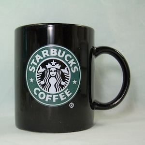 May include: A black ceramic coffee mug with a green Starbucks logo featuring a mermaid and the text "Starbucks Coffee".
