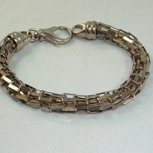 May include: A silver chain bracelet with a clasp closure. The chain is made of multiple rows of small, rectangular links.