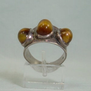 May include: Silver ring with three round tiger's eye stones set in a cluster. The ring is on a clear display stand.
