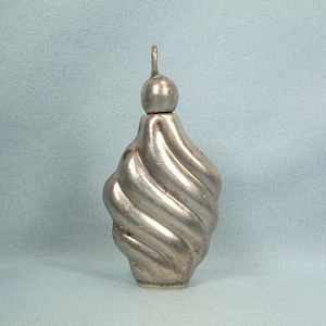 Pode incluir: Um frasco de perfume de prata em forma de espiral, com uma rolha redonda e um laço na parte superior para pendurar.