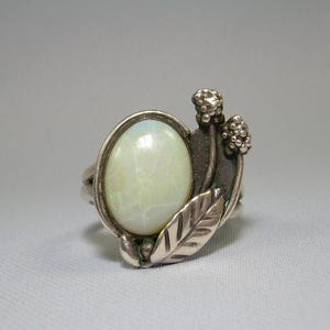 May include: A silver ring with a white opal stone and a floral design. The ring features a delicate leaf and two small flower buds.