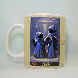May include: A white ceramic mug with a Star Wars themed design. The mug features a yellow background with an image of two Jawas from the Star Wars universe. The text "JAWA" is printed below the image.
