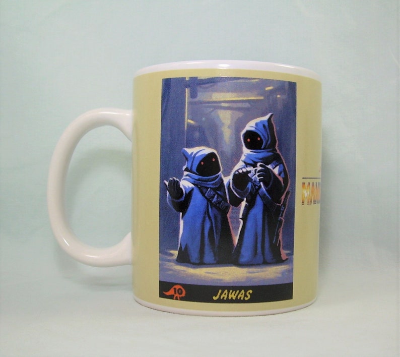 May include: A white ceramic mug with a Star Wars themed design. The mug features a yellow background with an image of two Jawas from the Star Wars universe. The text "JAWA" is printed below the image.