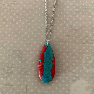May include: A silver chain necklace with a teardrop-shaped pendant made of red and blue stone.