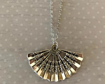 May include: A silver necklace with a decorative fan-shaped pendant. The pendant has a detailed design with intricate lines and curves.