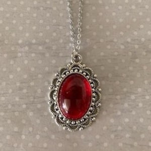 May include: A silver chain necklace with a red oval-shaped gemstone pendant set in a silver filigree frame.
