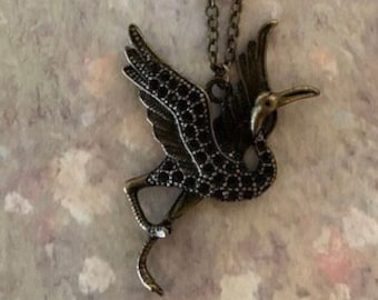 May include: A bronze necklace with a black jeweled crane pendant. The crane is in flight with its wings spread.