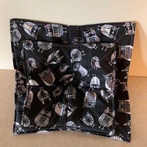 May include: Black and white owl print pot holder with a quilted design. The pot holder is folded in half and has a white stitching detail around the edges.