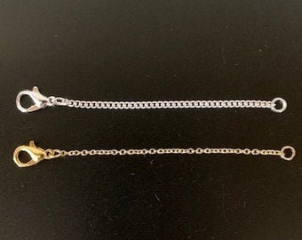 May include: Two silver chains with clasps, one gold chain with a clasp. The chains are on a black background.