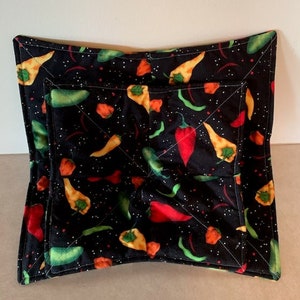 May include: A black quilted hot pad with a pattern of red, green, and yellow peppers on a black background with white speckles.
