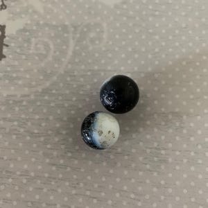 May include: Two small, round beads. One is solid black, and the other is white with a marbled black and gray pattern. The beads are displayed on a light gray surface with a white polka dot pattern.