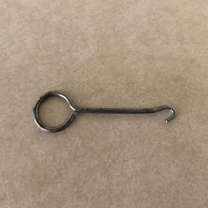 May include: A silver metal hook tool with a circular loop at one end and a hook at the other end.