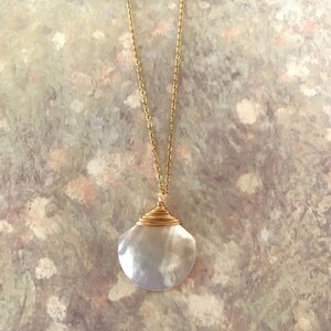 May include: A gold chain necklace with a white iridescent seashell pendant. The seashell is wrapped with gold wire.