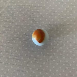 May include: A white marble with a swirl of orange and brown. The marble is round and smooth, with a glossy finish. This classic toy is perfect for collectors or for playing games.