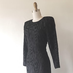 May include: Black vintage dress with long sleeves and a textured bodice. The dress features a flared skirt with a black tulle overlay adorned with gold-colored circles. The dress is displayed on a mannequin.
