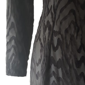 May include: A black dress with a unique pattern. The dress features a long sleeve and a textured design that resembles a zebra print. The fabric appears to be a soft, flowing material.