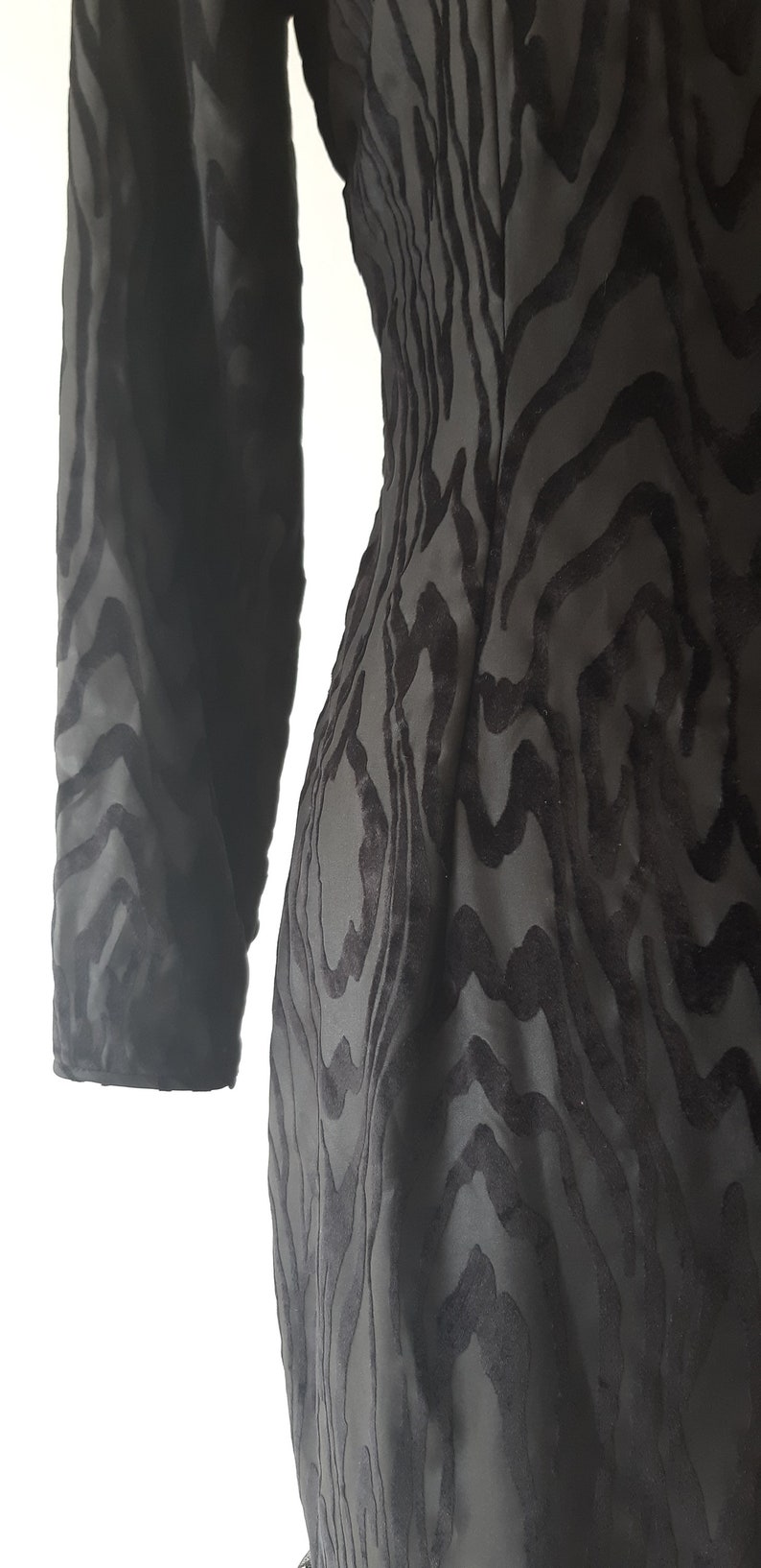 May include: A black dress with a unique pattern. The dress features a long sleeve and a textured design that resembles a zebra print. The fabric appears to be a soft, flowing material.