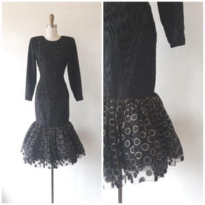May include: Black long-sleeve dress with a textured pattern. The dress features a fitted bodice and a flared skirt with a sheer overlay adorned with gold-colored circles. The dress is displayed on a mannequin.