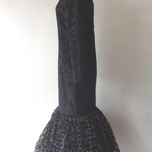 May include: A black dress with long sleeves and a textured pattern. The dress has a flared skirt with a pattern of gold circles on a black tulle base. The dress is displayed on a mannequin.