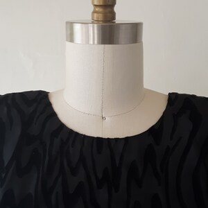 May include: A black top with a velvet zebra stripe pattern is displayed on a mannequin. The mannequin has a cream-colored neck and a gold-colored head. The top has a scoop neckline.
