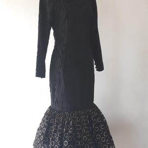 May include: Black vintage dress with long sleeves and a unique textured pattern. The dress features a fitted bodice and a flared skirt with a polka dot pattern. The dress is displayed on a mannequin.