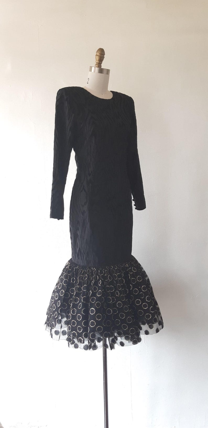 May include: Black vintage dress with long sleeves and a unique textured pattern. The dress features a fitted bodice and a flared skirt with a polka dot pattern. The dress is displayed on a mannequin.