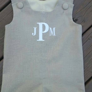 Może przedstawiać: Jaszek z jasnobrązowego lnu z białymi guzikami i haftowanym monogramem "JPM" z przodu.