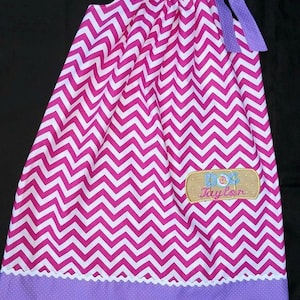 May include: A pink and white chevron patterned dress with a purple polka dot trim and a purple ribbon. The dress has a patch with the text "Doc Taylor" on it.