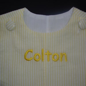 Puede incluir: Mono de bebé a rayas amarillas y blancas con el nombre "Colton" bordado en hilo amarillo.