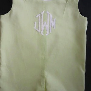 Puede incluir: Un pelele verde claro sin mangas con botones blancos y un monograma bordado blanco "JWM" en la parte delantera.