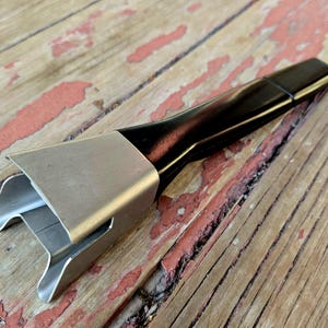 May include: A black and silver pot handle with a unique design. The handle is made of metal and has a black rubber grip.