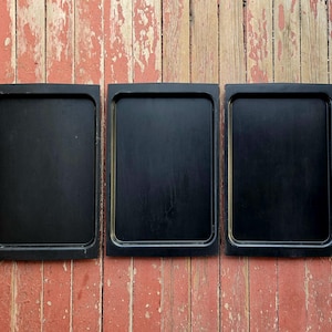 May include: Three black rectangular trays with a raised edge, hanging on a red wooden wall.