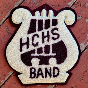 May include: A white and maroon felt patch with a lyre design. The text "HCHS BAND" is embroidered on the patch.