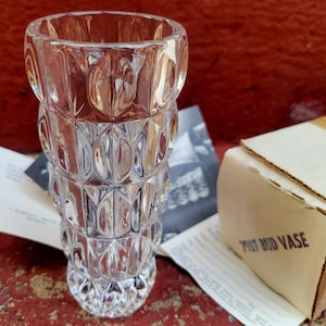 Könnte beinhalten: Eine klare Glas-Blumenvase mit geometrischem Muster. Die Vase steht auf einem Tisch mit einer weißen Box, auf der "7007 BUD VASE" steht.