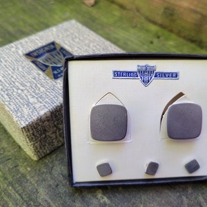 May include: A black box with a white interior containing four sterling silver cufflinks. The box has a label that reads "Sterling Silver" with a shield design.