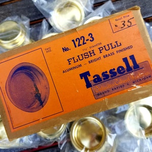 May include: A box of 1 1/2 inch diameter flush pull cabinet hardware. The box is orange and brown with the text "No. 122-3 FLUSH PULL ALUMINUM - BRIGHT BRASS FINISHED Tassell Distinctive Cabinet Hardware GRAND RAPIDS 4, MICHIGAN" printed on it. The retail price is £0.35.