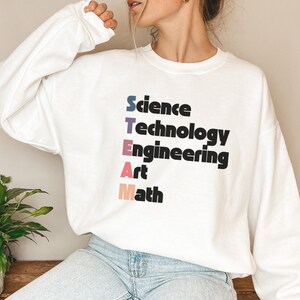 May include: White sweatshirt with the acronym "STEAM" spelled out vertically in colorful letters. The letters stand for Science, Technology, Engineering, Art, and Math.
