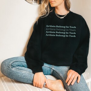 May include: Black sweatshirt with the text "Artists Belong In Tech" repeated four times in a gradient font.